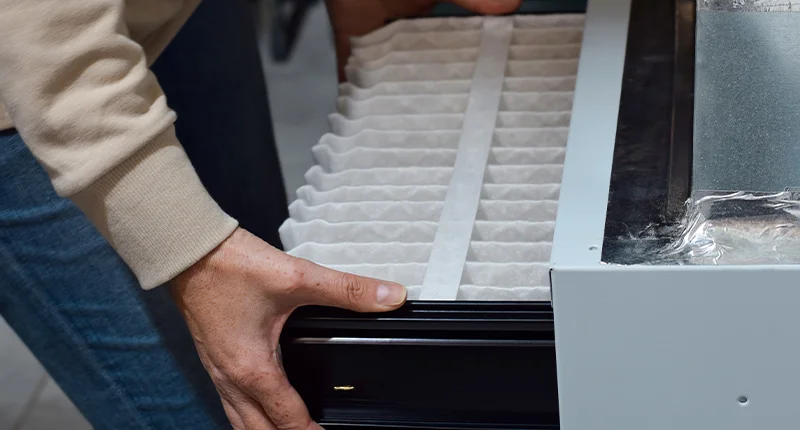 A homeowner removes an air filter from a furnace during maintenance