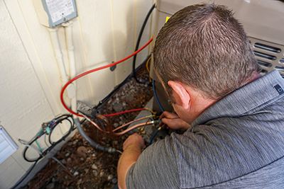 A heating and cooling technician from Bill's heating and AC is brazing an air conditioning condenser line set.