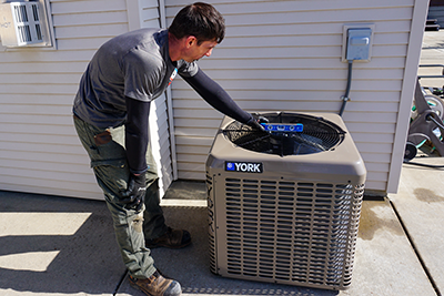 An air conditioning technician is finishing an install of a condenser by leveling it.
