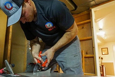 A Bill's Heating employee is cutting a heating furnace to connect ductwork to it.