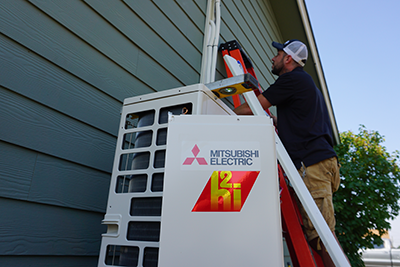 A Bill's Heating employee is installing line hide for a mitsubishi hyper heat ductless heat pump which can be seeen in the foreground..