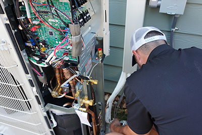 A heat pump technician is finishing an install of a condenser by connecting the line set.