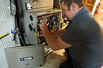 A furnace technician is using tools to finish the installation of a high efficiency gas furnace.