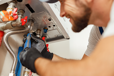 A plumber is unscrewing a panel on a tankless water heater.